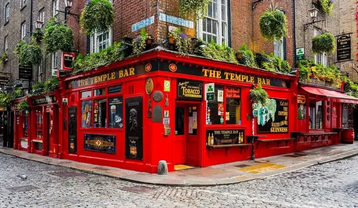 The bright red facade of The Temple Bar, a corner pub on a cobblestone street, adorned with lush hanging green plants.