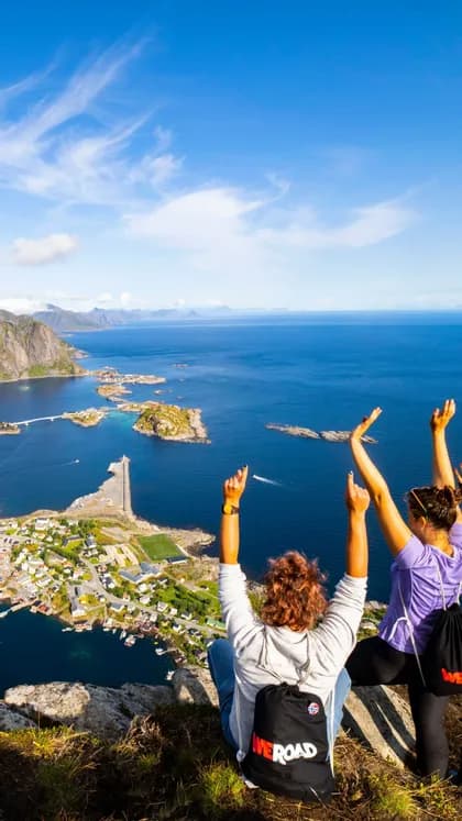Deux personnes lors d'un voyage en groupe WeRoad, les bras levés, dominant un village côtier depuis une falaise.