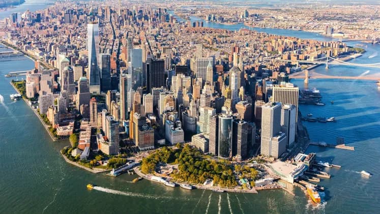 Vue aérienne de la ligne d'horizon de Lower Manhattan, avec des gratte-ciel denses entourés de rivières par une journée ensoleillée.