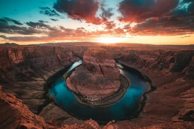 Un'ampia vista di un fiume che si snoda in un canyon di roccia rossa sotto un cielo al tramonto colorato.