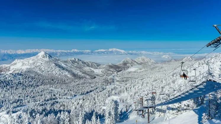 Ein Panoramablick vom Sessellift zeigt eine weite Landschaft aus schneebedeckten Bergen und Wäldern unter strahlend blauem Himmel.