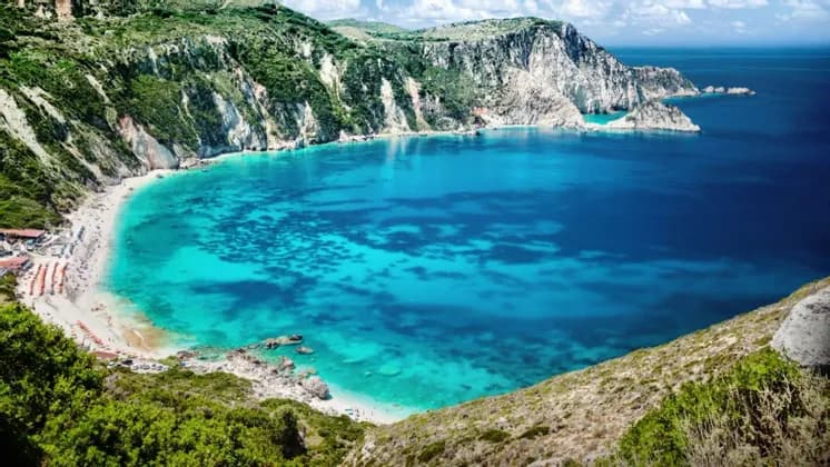 Una vista dall'alto di una cala appartata con acqua turchese, una spiaggia sabbiosa con persone e ripide scogliere verdi e bianche.