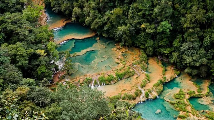 Eine Luftaufnahme von gestuften türkisfarbenen Wasserbecken und Wasserfällen, die durch einen dichten grünen Wald fließen.