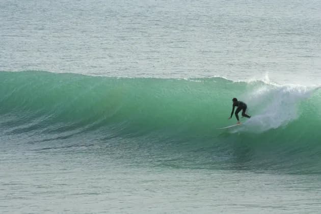 A surfer in a black wetsuit rides a surfboard on a large, green wave in the ocean.