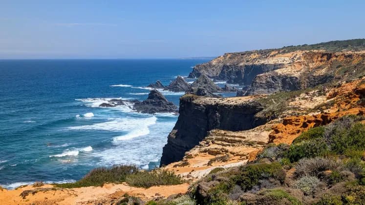 Eine zerklüftete Küste mit steilen Klippen und Felsnadeln, die unter klarem Himmel aus dem blauen Ozean ragen.