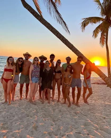 Un grupo de WeRoad posa en una playa de arena con palmeras al atardecer sobre el océano.