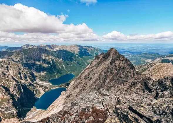 Une vue panoramique depuis un sommet rocheux dominant une vaste chaîne de montagnes avec deux lacs alpins bleus dans une vallée en contrebas.