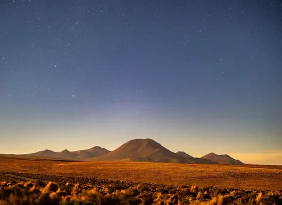 Una vasta pianura desertica con montagne ondulate in lontananza sotto un cielo notturno limpido e stellato.