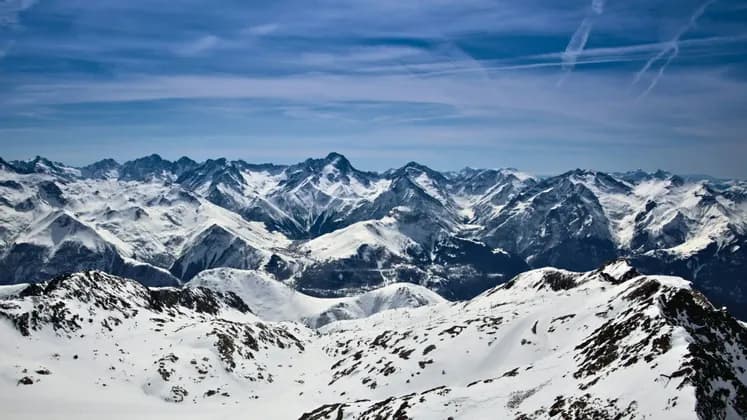 Ein Panoramablick auf eine weite, schneebedeckte Bergkette mit zerklüfteten Gipfeln unter einem klaren blauen Himmel.