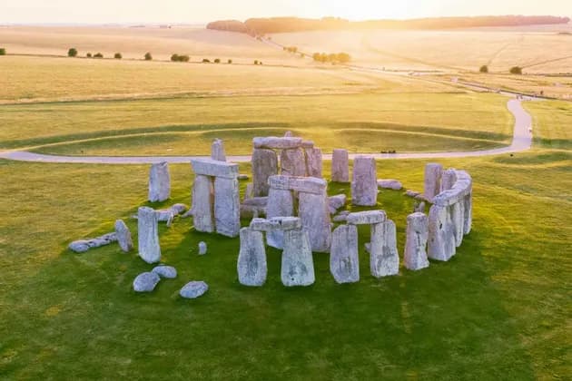 Una vista aerea del monumento di Stonehenge su un prato verde, illuminato dalla luce dorata del tramonto su campi ondulati.