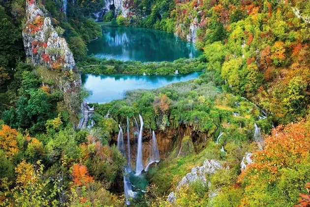 Des cascades se déversent dans des lacs turquoise, entourés d'une forêt dense aux couleurs automnales.