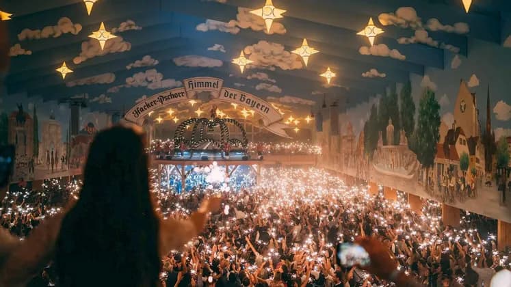 A large crowd holds up glowing sparklers inside a festive hall with a painted ceiling and star-shaped lights.