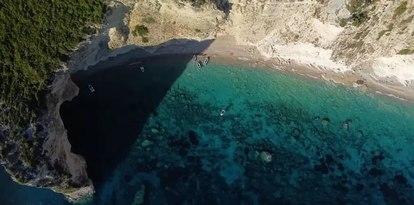 Une vue aérienne d'une crique isolée où de petits bateaux sont amarrés sur la plage et flottent dans la mer turquoise cristalline à côté de falaises abruptes.