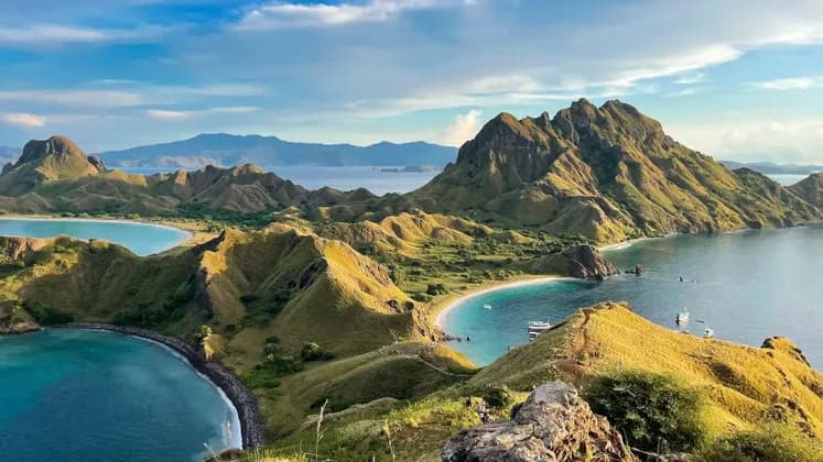 Una vista panoramica da una collina su isole verdi ondulate, baie turchesi e spiagge di sabbia bianca sotto un cielo nuvoloso.