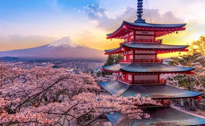 Eine rote Pagode steht inmitten blühender Kirschbäume und überblickt bei Sonnenuntergang eine Stadt mit einem schneebedeckten Berg in der Ferne.