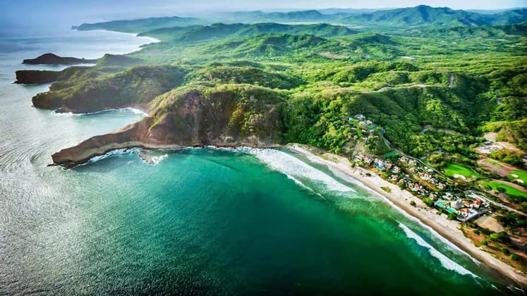 Veduta aerea di una vibrante costa verde con acqua turchese che lambisce una spiaggia sabbiosa e scogliere.