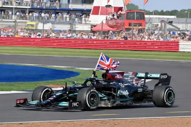 A black Formula 1 race car with a British flag attached drives around a track in front of spectators in the stands.