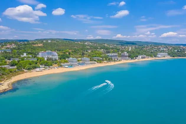 Vista aerea di due moto d'acqua su acque turchesi, vicino a una spiaggia sabbiosa con hotel e colline verdi.