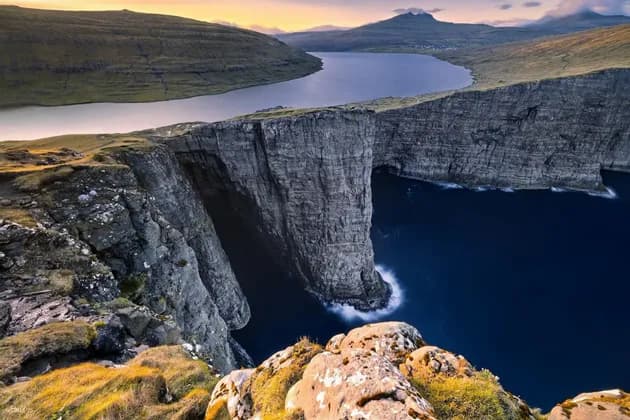 Un grande lago si trova sul bordo di un'alta scogliera, affacciato sul profondo oceano blu, con verdi colline ondulate in lontananza.