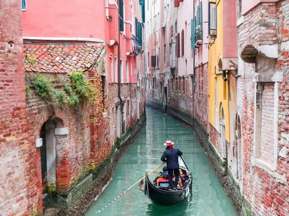 Un gondolier rame une gondole le long d'un canal étroit bordé de bâtiments en briques colorées.