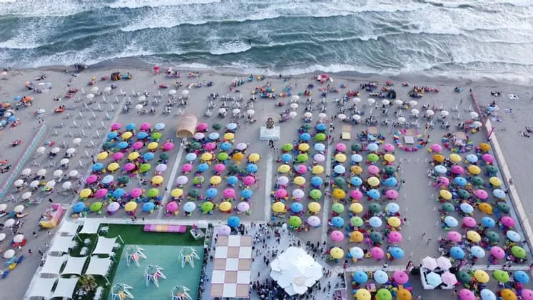 Vista aerea di una spiaggia affollata con file di ombrelloni colorati disposti sulla sabbia accanto al mare.