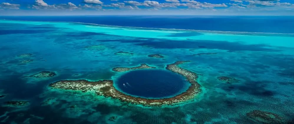 Una vista aerea di un grande, profondo buco blu marino circolare, circondato da un atollo di barriera corallina in un oceano turchese.