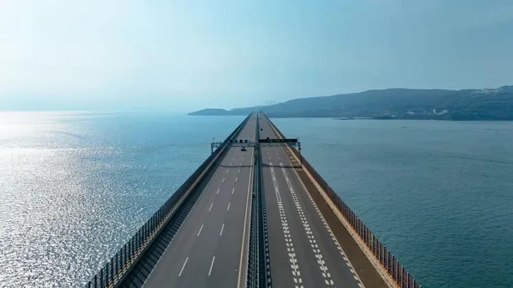 A long highway bridge extends over the sea towards a distant, hazy shoreline.