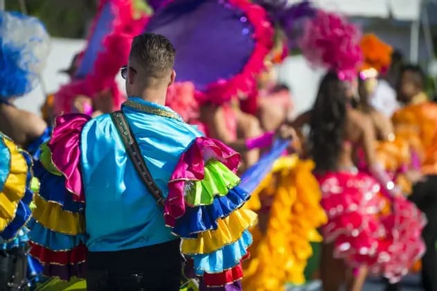 Vista posteriore di un uomo con una camicia blu brillante e maniche a balze colorate, parte di un viaggio di gruppo WeRoad durante una sfilata di carnevale.