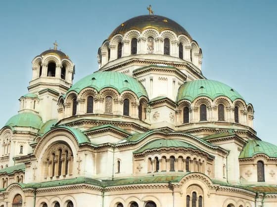 A large cathedral with a central golden dome and multiple green domes against a clear blue sky.