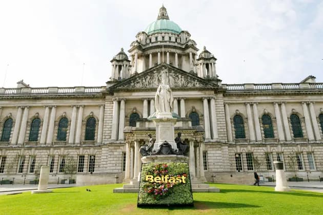 Un'insegna floreale 'Belfast' e una statua sul prato davanti al grandioso Municipio di Belfast.