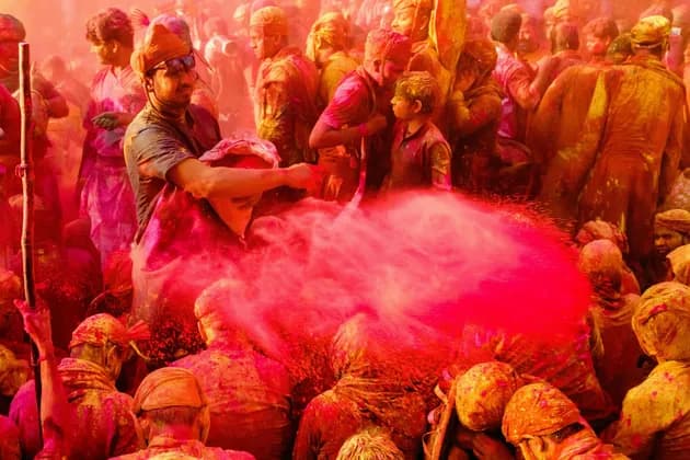 Un uomo con il turbante lancia una nuvola di polvere rossa su una fitta folla di persone, anch'esse ricoperte di polvere colorata.