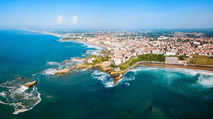 Veduta aerea di una città costiera, con una lunga spiaggia sabbiosa e una costa rocciosa che si affaccia sull'oceano blu.