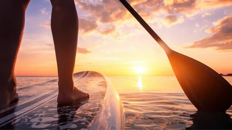 Vista dal basso di una persona che fa stand-up paddle sul mare calmo durante un tramonto vibrante.