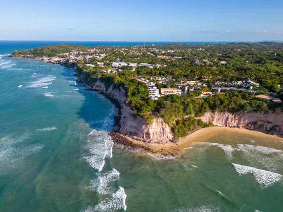 Una vista aerea di una città costiera su scogliere rossastre, con vegetazione rigogliosa, una spiaggia sabbiosa e l'oceano turchese sottostante.