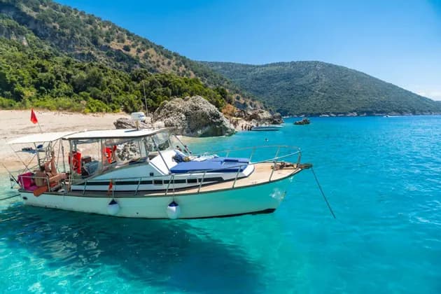 Un gruppo WeRoad si rilassa su una barca ancorata in acque calme e turchesi, vicino a una spiaggia con lussureggianti colline verdi.
