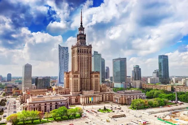 Vista aerea di un grattacielo storico circondato da edifici moderni in un centro città sotto un cielo parzialmente nuvoloso.