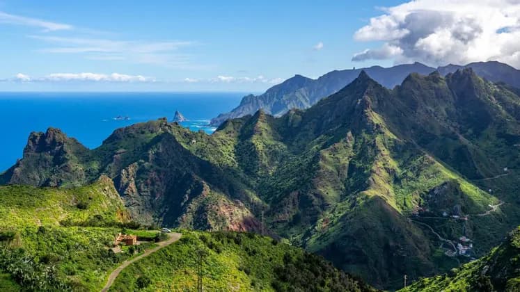Una vista panoramica e ampia di aspre montagne verdi lungo una costa, che si uniscono a un mare blu intenso sotto un cielo parzialmente nuvoloso.
