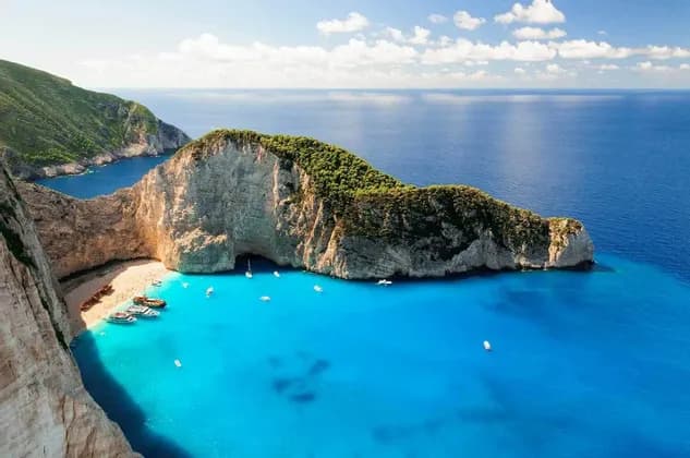 Una vista aerea di una cala appartata con un relitto su una spiaggia di sabbia bianca, circondata da scogliere e acqua turchese con barche.
