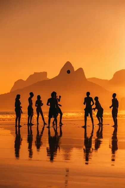 Un viaggio di gruppo WeRoad si staglia giocando a palla su una spiaggia bagnata al tramonto, con le montagne sullo sfondo.