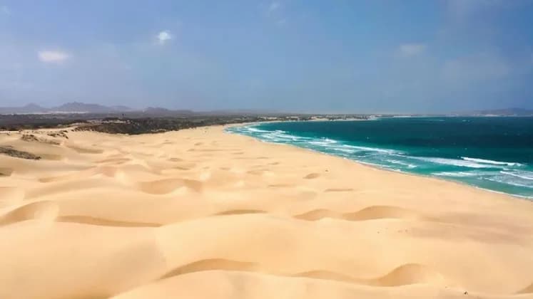 Vastas dunas de arena dorada descienden hasta el encuentro de las olas turquesas del océano a lo largo de una extensa costa.