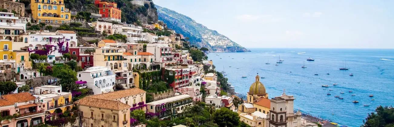 Una vista panoramica di una colorata città costiera costruita su una scogliera, che si affaccia su un mare blu con tante barche.