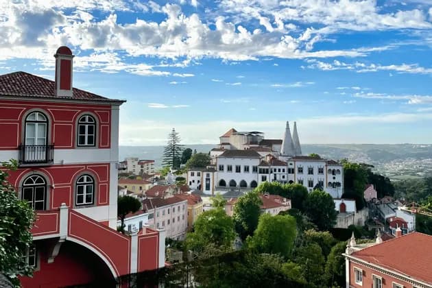 A view over a historic town with colorful buildings, including a palace with two large conical chimneys, under a blue cloudy sky.