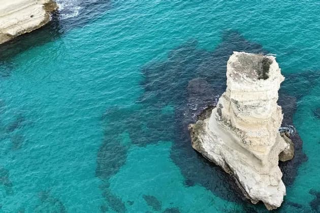 Una vista aerea di un faraglione alto e bianco che si erge in acque oceaniche turchesi e vibranti, accanto a una scogliera.