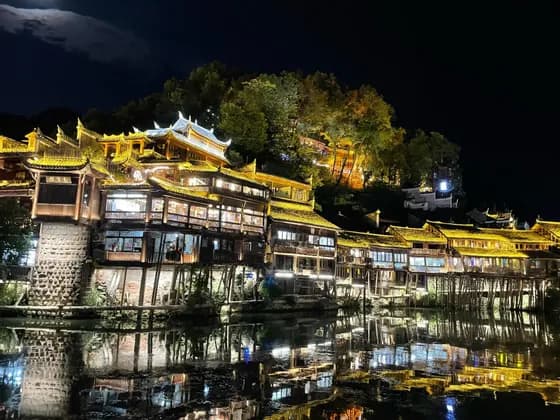 Case su palafitte tradizionali illuminate che si riflettono in un fiume di notte sotto una luna splendente.