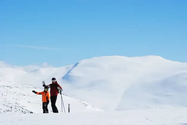 Un viaggio di gruppo WeRoad con due persone in tenuta da sci che salutano da una montagna innevata sotto un cielo azzurro e limpido.