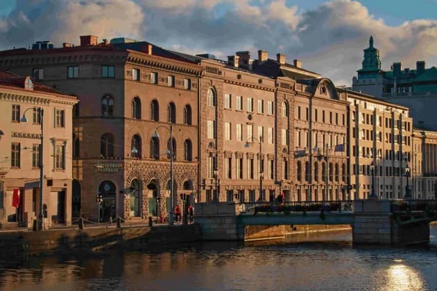 Sunlight during the golden hour illuminates ornate buildings lining a city canal, with reflections in the water.