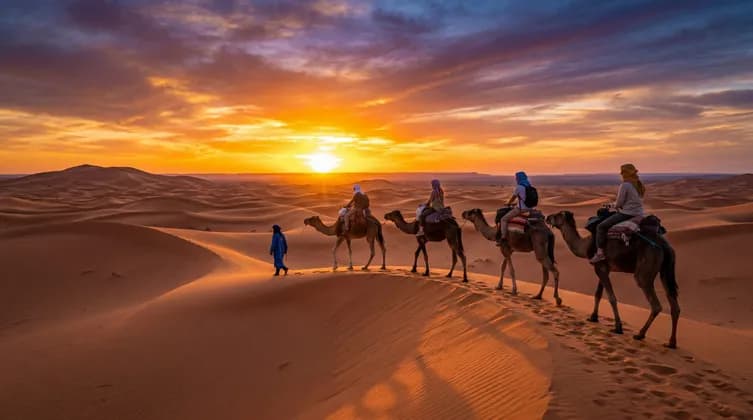 Ein Guide führt eine WeRoad Gruppenreise auf einer Kamelkarawane über weite Sanddünen bei Sonnenuntergang.