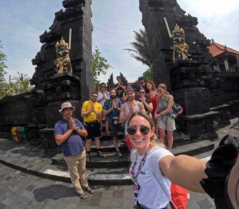 Un voyage de groupe WeRoad prend la pose pour un selfie avec un guide, faisant un geste de prière devant une porte traditionnelle en pierre noire.