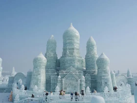Un imponente castello con torri e cupole scolpite nel ghiaccio, con visitatori che passeggiano intorno nella neve.