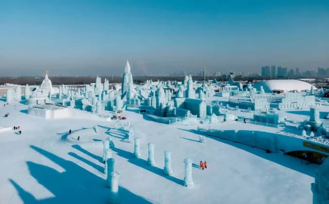Una veduta aerea di una vasta città tentacolare, con castelli ed edifici interamente scolpiti nel ghiaccio e nella neve, il tutto sotto un cielo azzurro e sereno.